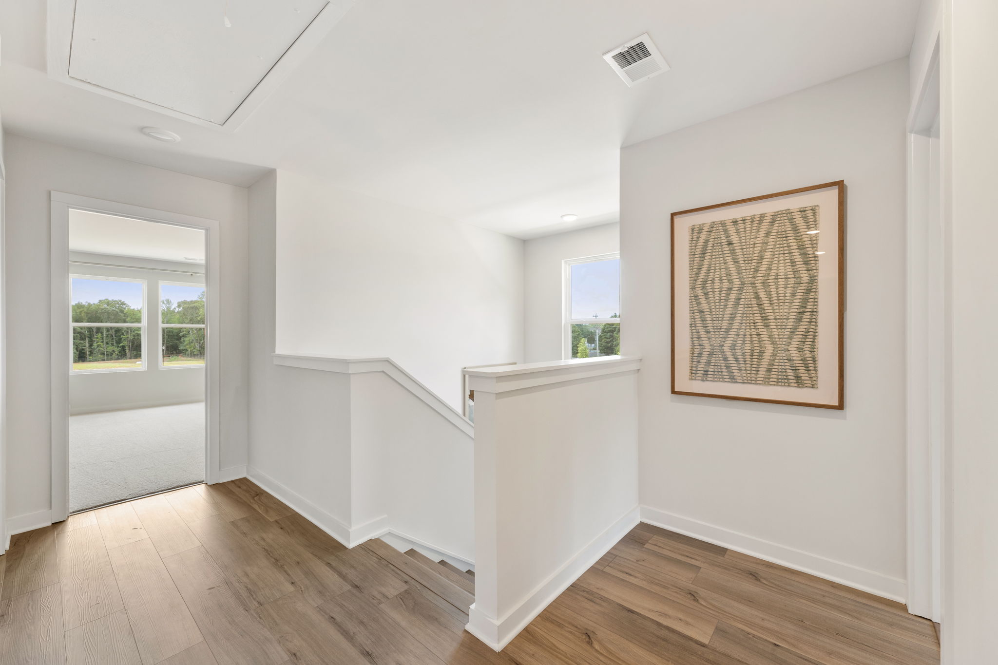A room with a wood floor and a white wall with a painting on it.