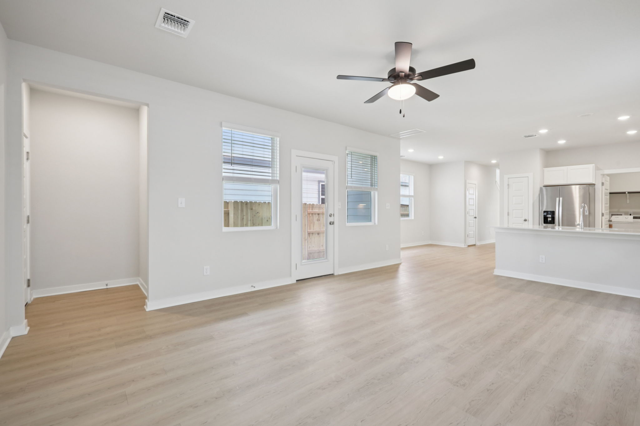 A large empty room with a ceiling fan and white cabinets.