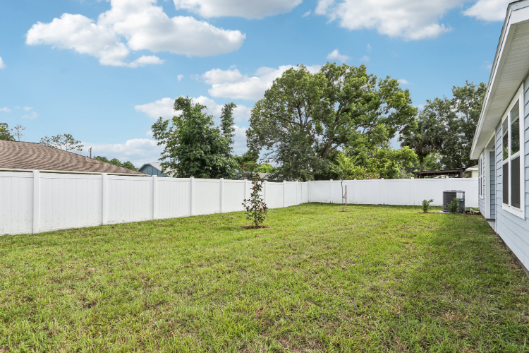 A yard with a white fence and trees in the background.